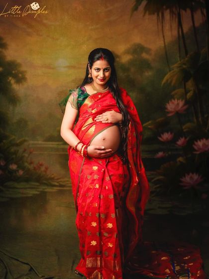 A beautiful mom-to-be in a traditional red saree against a painted backdrop of a serene lake. This is a classic fine art maternity portrait.