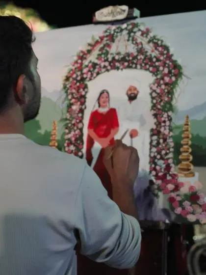 Adding the fine details to the bride's red lehenga. We work diligently through the event to complete the painting by the end.