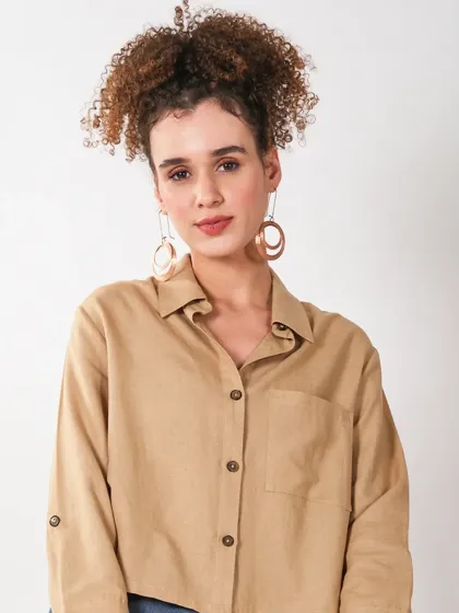 A close-up portrait of a model in a beige button-up shirt, focusing on the texture of the fabric and the model's confident expression.