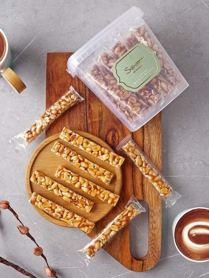 Sweet, crunchy, and packed with protein. My Peanut Chikki, made with jaggery, is the perfect snack to fuel your day, shown here with coffee and in convenient packaging.