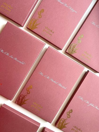 A wider shot of the calligraphed invitation boxes. The white ink provides a soft, elegant contrast against the dusty rose color.
