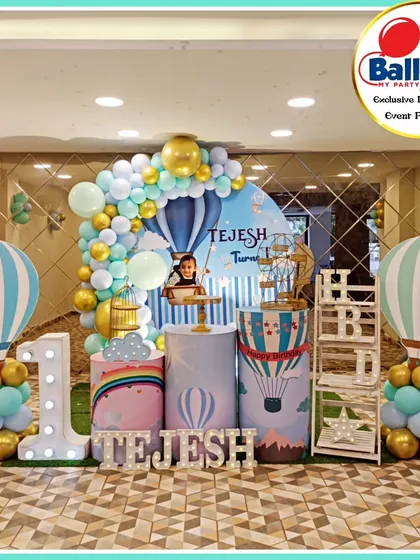 A charming hot air balloon-themed first birthday. The setup includes hot air balloon cutouts, a 'TEJESH' marquee, and a large light-up number '1'.