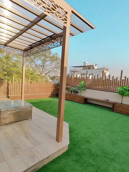 A wide view of the golden pergola, showing how it defines the seating area on the lush artificial lawn.
