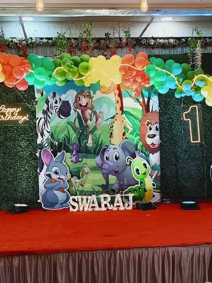 A jungle-themed first birthday stage with a green grass wall and colorful balloon arch.