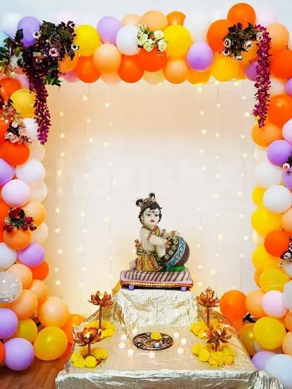 This is a simple yet beautiful decoration for a home Janmashtami puja. I created a colorful balloon frame with small floral details and a backdrop of warm fairy lights to highlight the Bal Krishna idol, making a perfect little mandap at home.