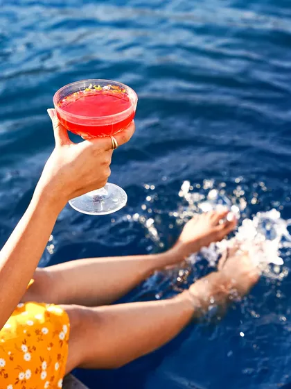 A woman's hand holds a bright red cocktail against the backdrop of deep blue water. This shot evokes a sense of summer vacation, relaxation, and poolside luxury.