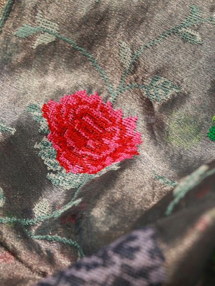 A close-up of the vibrant red rose embroidered on the grey tissue silk.