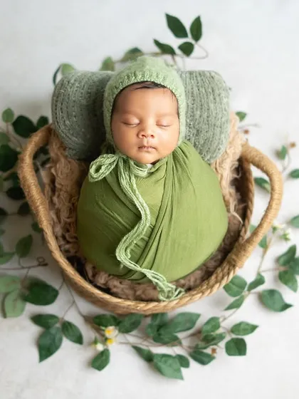 A newborn boy nestled in a basket with lush green wraps and ivy. This nature-inspired setup is perfect for creating a calm and organic feel.