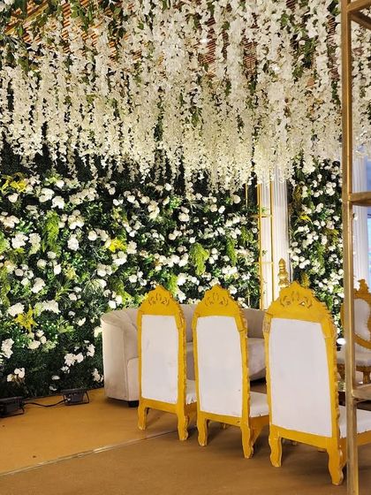 A lush green and white themed Vidhi setup inside a banquet hall. The stage features a dense floral wall and a ceiling of hanging wisteria, creating an indoor garden effect.
