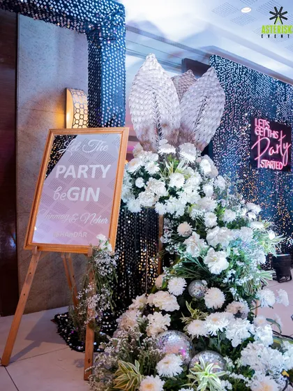 The entrance to the cocktail party, with a sequin backdrop, a fun "Let the Party beGin" sign, and lush white floral arrangements.