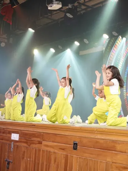 A wide shot of our students in their neon yellow overalls during the 'ON STAGE 26' showcase. The professional stage setup with dramatic lighting gives them a true taste of being a star.