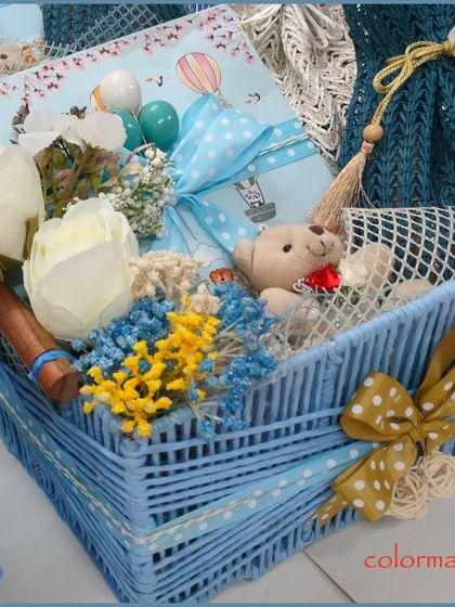A beautiful baby boy hamper in a woven blue basket. This gift is carefully assembled with a teddy bear, floral accents, and other newborn essentials, all tied together with a charming blue polka-dot ribbon.