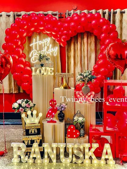 A vibrant red-themed birthday surprise. This setup features a heart-shaped balloon arch, a "Happy Birthday" neon sign, and the name "Ranuska" in marquee letters for a bold and personal touch.