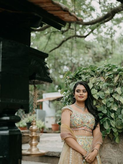 A bride in a light green lehenga, standing near a temple-like structure, a picture of grace and elegance.