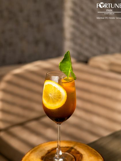 An elegant iced tea or cocktail, garnished with a slice of lemon and a fresh leaf, catching the afternoon sun.