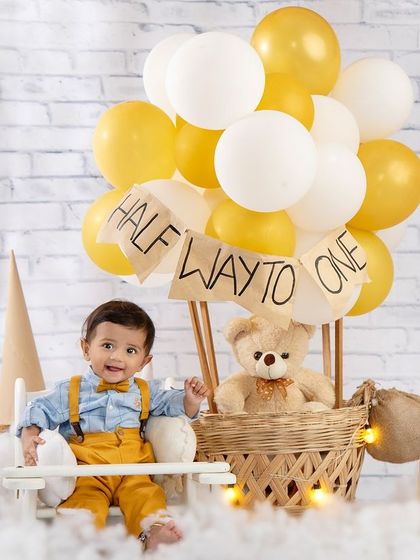 Halfway to one and soaring high! A little pilot and his teddy bear co-pilot are ready for takeoff in their hot air balloon.