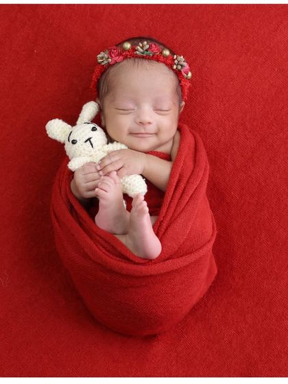 A heart-melting sleepy smile. This baby girl, wrapped in red and holding a small bunny, creates a perfectly sweet and simple portrait.