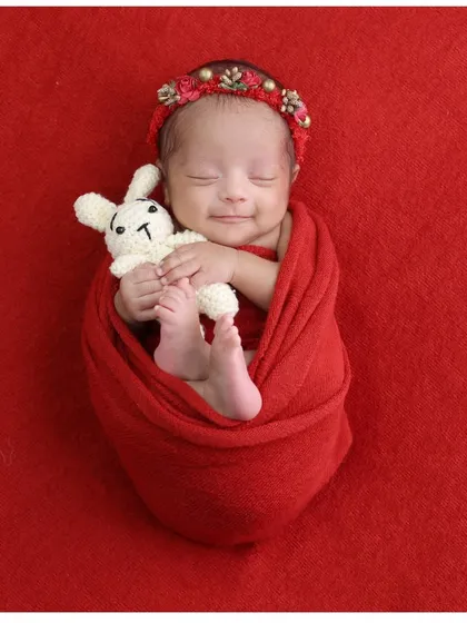 A heart-melting sleepy smile. This baby girl, wrapped in red and holding a small bunny, creates a perfectly sweet and simple portrait.