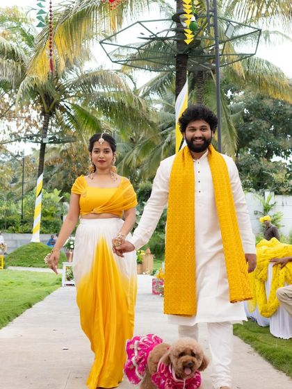 A couple walking hand-in-hand with their furry friend. Their coordinated yellow and white outfits are stylish and comfortable, perfect for an outdoor event.