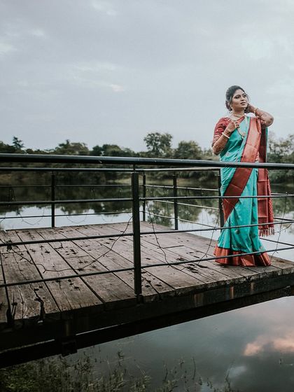 A serene portrait of the bride-to-be in a beautiful saree, standing on a wooden dock overlooking the water during her engagement shoot.