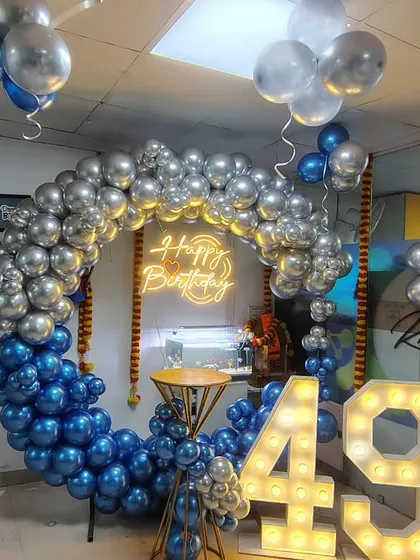 An office celebration for a 49th birthday. We set up this full circle balloon ring using metallic blue and silver chrome balloons for a sleek look. The large, illuminated '49' marquee numbers and the bright 'Happy Birthday' neon sign created a fantastic photo corner for the team.