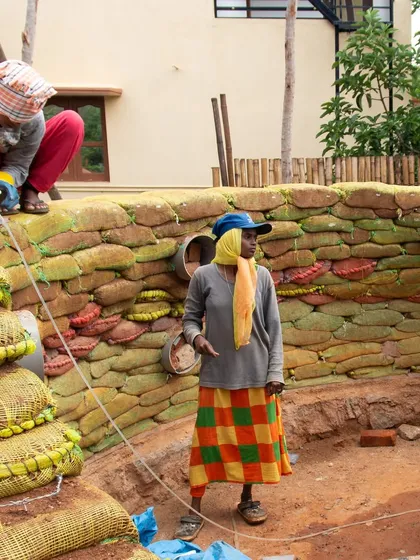 Women masons constructing a wall using earthbags and incorporating bottle-ends for decoration. This project transforms perceptions of traditional architecture while empowering the women who build it.