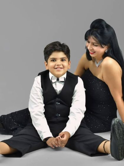 A stylish mother and son portrait. They are dressed in elegant black outfits and sitting together on the floor of the studio, sharing a sweet, connected moment.