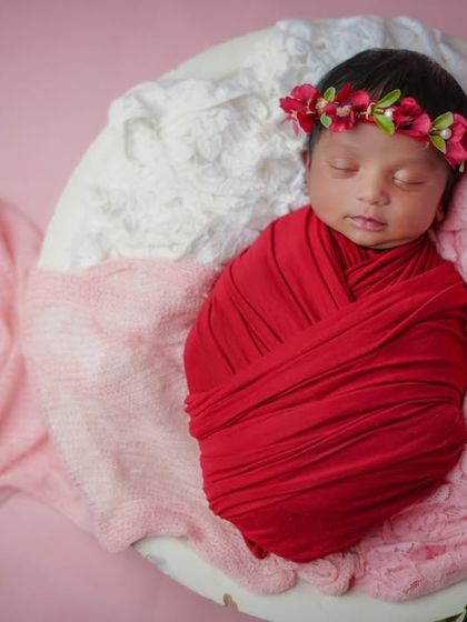 A little rosebud. Swaddled in red and wearing a floral crown, this baby is the picture of newborn beauty.