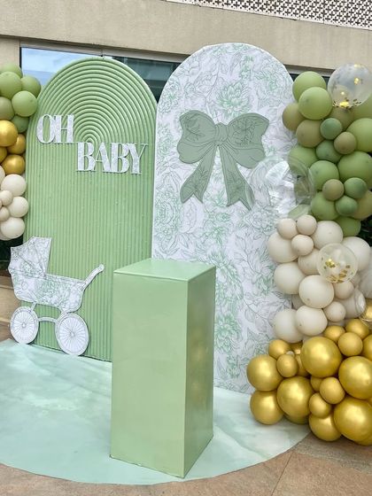 A full view of the sage green 'Oh Baby' shower backdrop. The addition of gold and white balloons adds a touch of glamour to the modern and minimalist design.