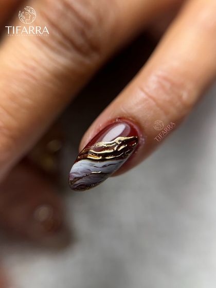 A close-up of a rich burgundy and white marble nail, accented with textured gold chrome for a dramatic and opulent look.