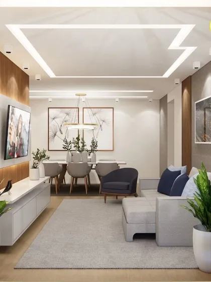 A spacious living and dining area with a unique L-shaped false ceiling design. The neutral color palette is accented with pops of blue and green.
