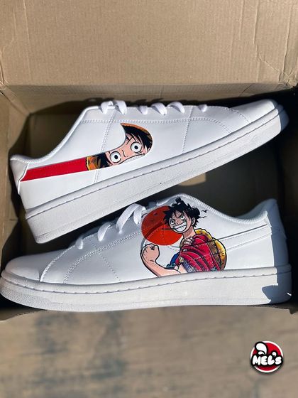 An unboxing view of the complete One Piece custom Nike sneaker set. You can see both the Luffy portrait shoe and the peeking-face swoosh shoe together, making for a perfect pair.
