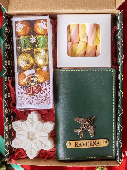 A close-up of the Christmas corporate gift box. It contains a personalized passport holder, festive chocolates, marshmallows, and a snowflake-shaped candle, all packed in a holiday-themed box.