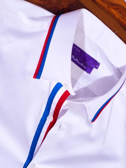 A crisp white shirt with a twist. This piece features a bold red and blue striped lining on the collar and placket for a pop of color.