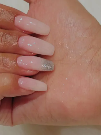 A close-up of a single nail from a beautiful ombré set. You can see the subtle transition from pink to white, with a delicate silver glitter tip for a touch of sparkle.