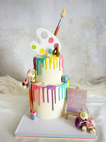 A cake for a little artist! This two-tier art-themed cake features colorful drips, a painter's palette, and paintbrushes.