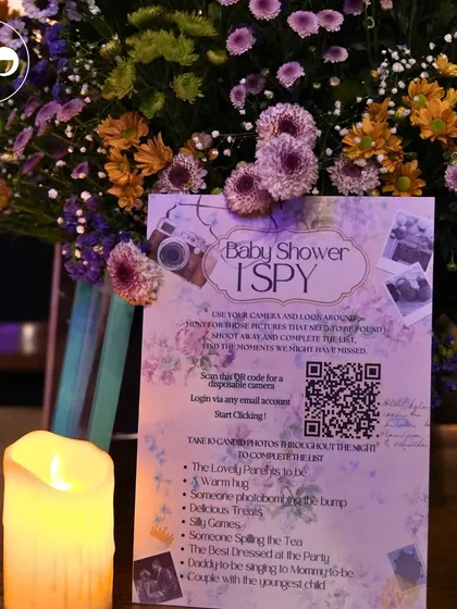 A 'Baby Shower I Spy' game card with a QR code for a digital disposable camera. This is a modern and fun way to get guests to capture candid moments throughout the event.