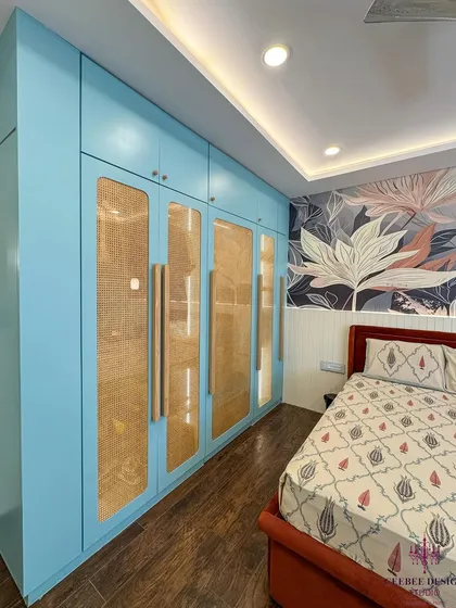 A bedroom with light blue wardrobes featuring rattan panels and a bold floral wallpaper accent wall.