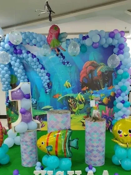 An aquarium-themed birthday party with an underwater backdrop. The setup includes foil balloons shaped like a fish, seahorse, and octopus.