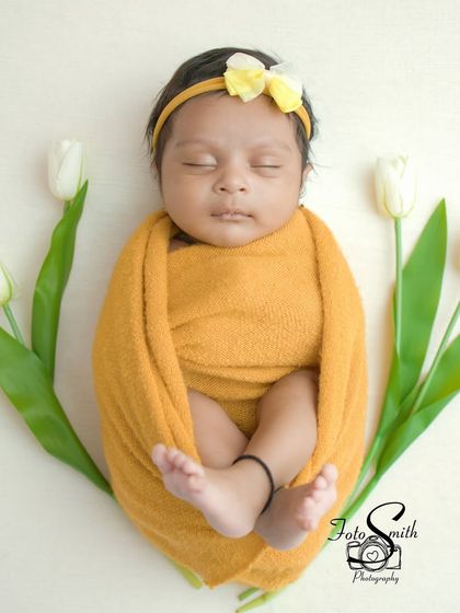 A baby swaddled in a warm yellow wrap, sleeping peacefully. The white tulips on either side create a simple, elegant, and balanced composition.
