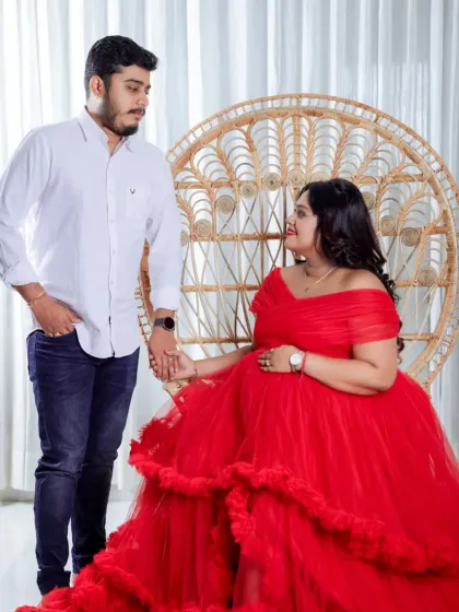 A romantic moment in our studio, with the mom-to-be seated in the peacock chair. The vibrant red gown and the couple's connection make this a standout shot.