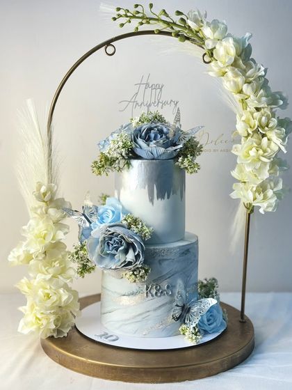 This two-tiered anniversary cake, with its marble-effect fondant and silver-dusted sugar flowers, is presented on a floral arch stand for an extra touch of elegance.