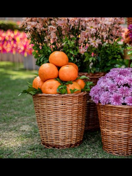 A close-up of a wicker basket filled with fresh oranges, placed next to a basket of pink chrysanthemums.