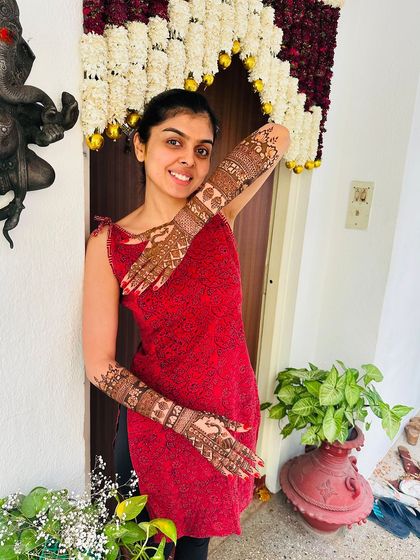 A happy bride in a red dress, posing playfully to show her full-arm mehndi.