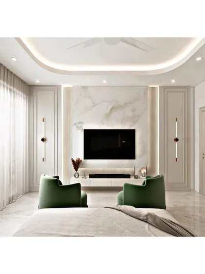 We create bedrooms that feel both grand and serene. This room features a full-height marble-clad TV wall, elegant wall paneling, and integrated cove lighting in the false ceiling. The plush green armchairs add a pop of color and sophistication.