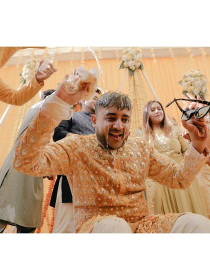 A groom gets doused with water by his friends during a playful moment at his haldi ceremony.