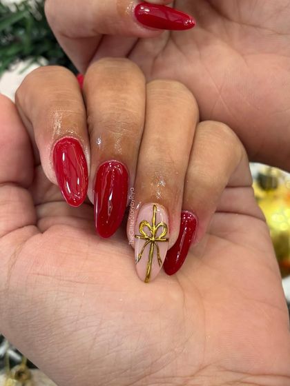 A classic and bold Christmas manicure. This set features glossy red nails with a single accent nail on each hand with a hand-painted gold bow.