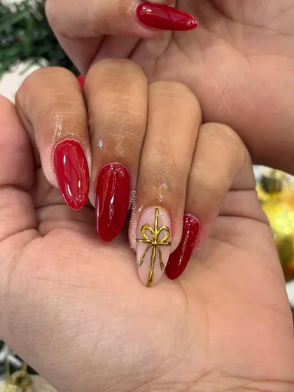 A close-up of the gold bow accent nail, showing the intricate, hand-painted detail on a nude base.