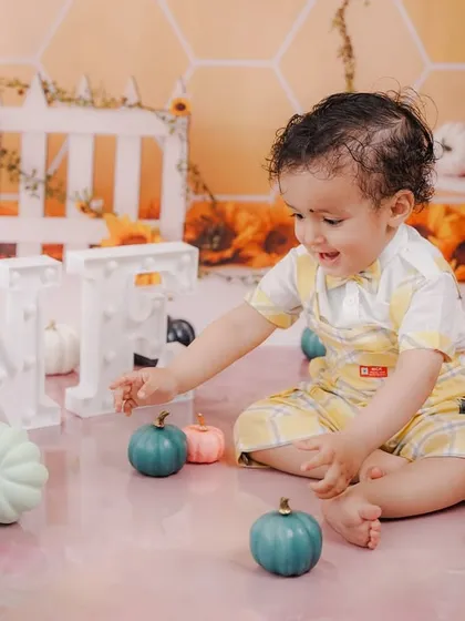 Interacting with the "ONE" sign and colorful pumpkins, this shot is full of life and captures the curiosity of a one-year-old.
