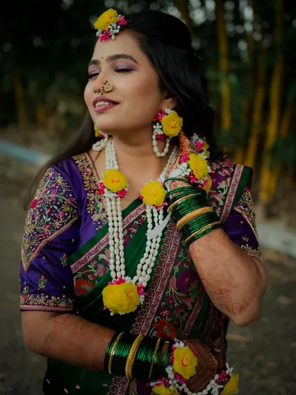 The Haldi glow is real. This bride, with her eyes closed in a moment of bliss, looks absolutely serene, adorned with fresh flower jewelry that complements her green and purple saree.